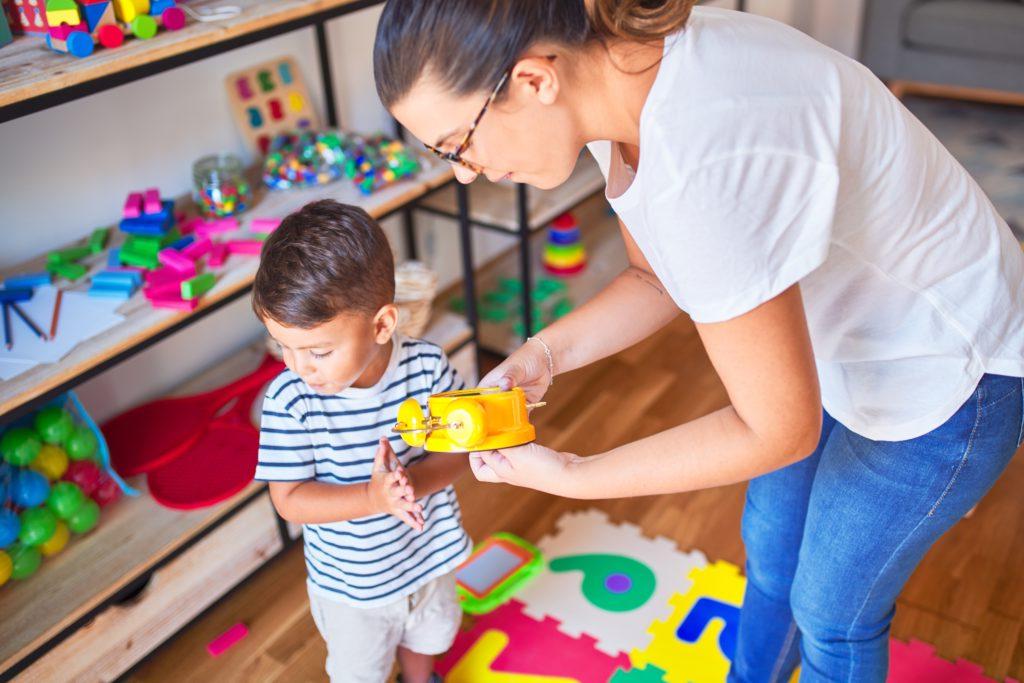 A teacher showing a young boy a colorful alarm clock in a classroom.